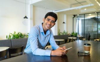 A young man sitting at a table with his phone, focusing on personality development.